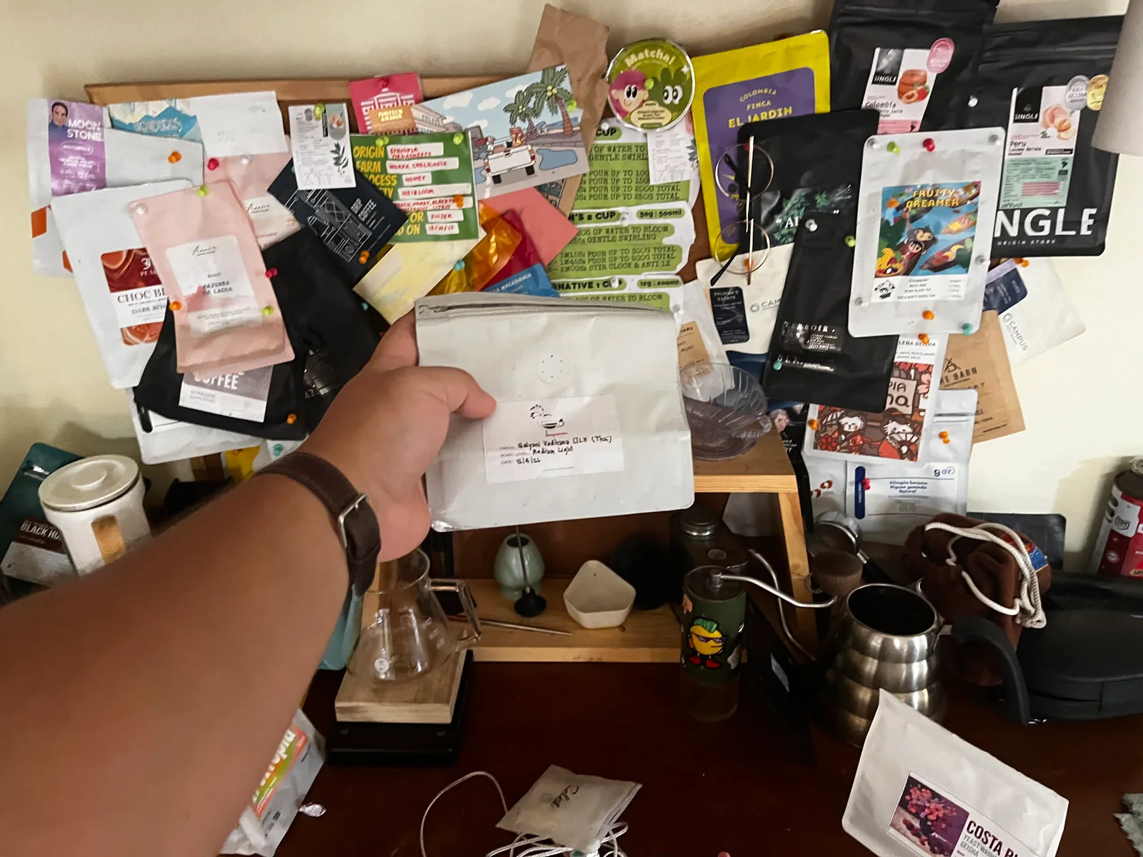 A coffee bag held in front of a wall of saved coffee packaging and brewing gear